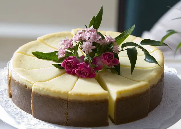 A cheesecake with pink flowers and green leaves on top. The cake is cut into slices.