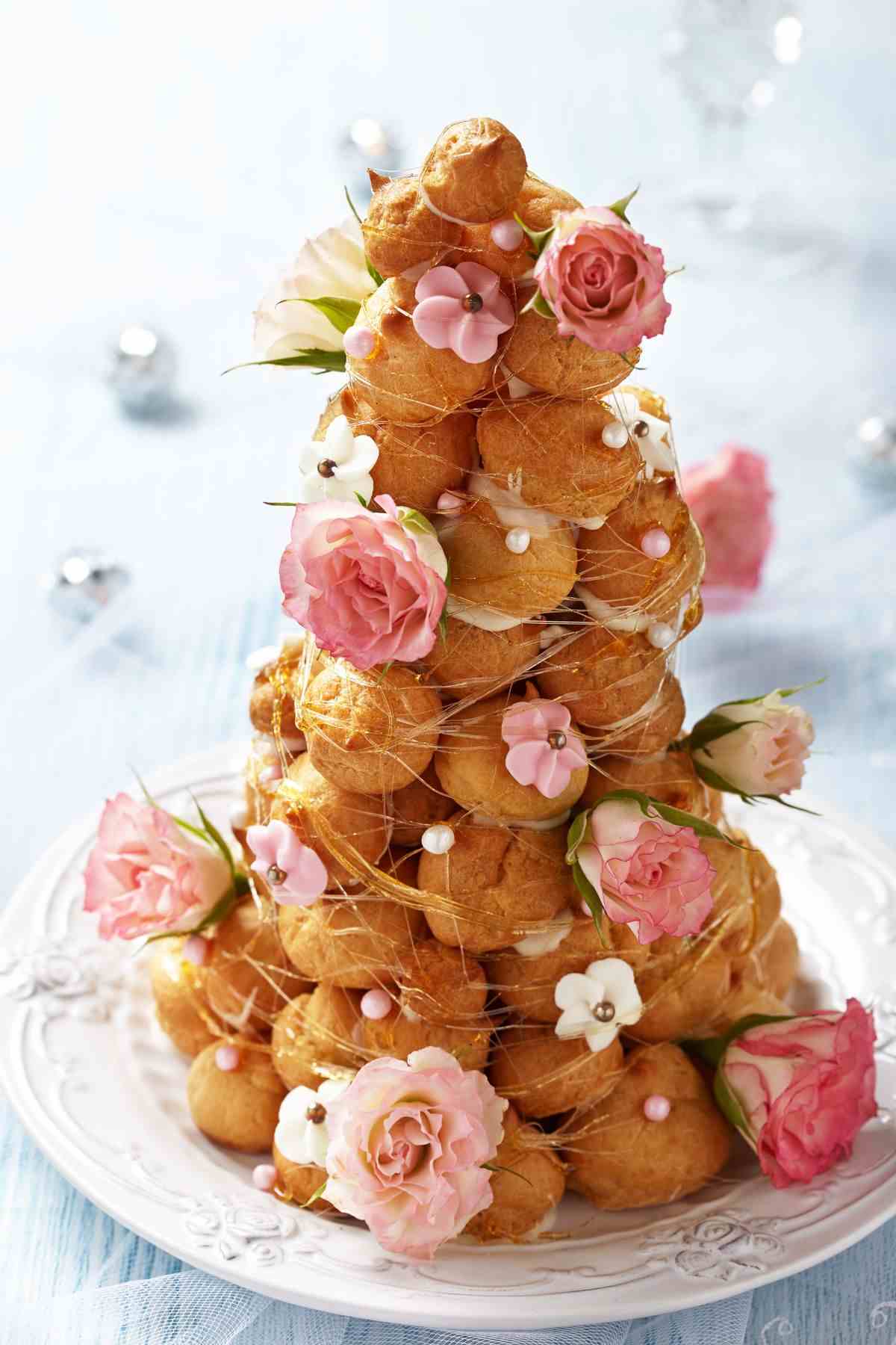 A tall croquembouche decorated with pink roses and white flowers on a white plate.