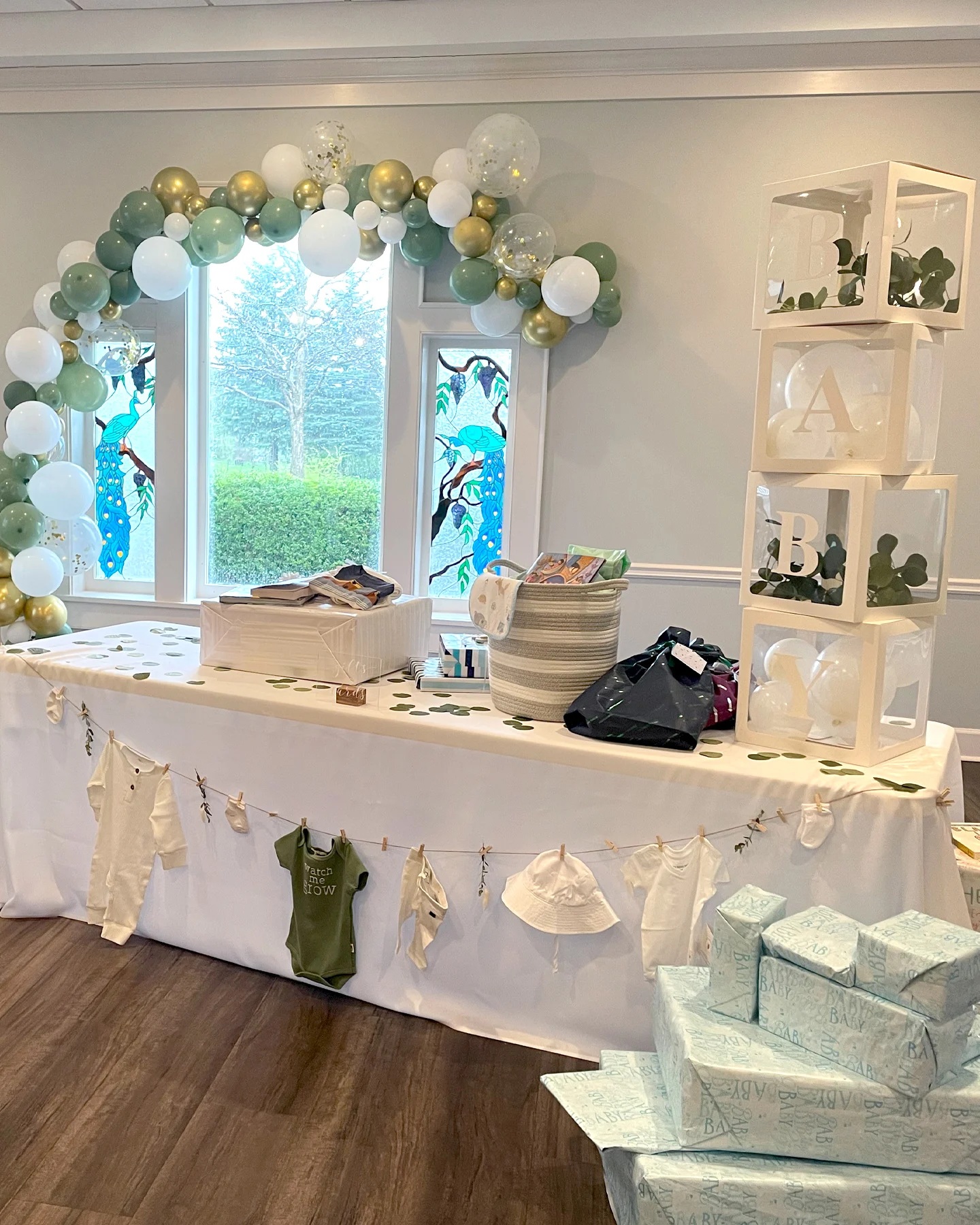 A beautifully decorated baby shower table with white and green decorations. The table has a white tablecloth and is set up with gifts and treats.