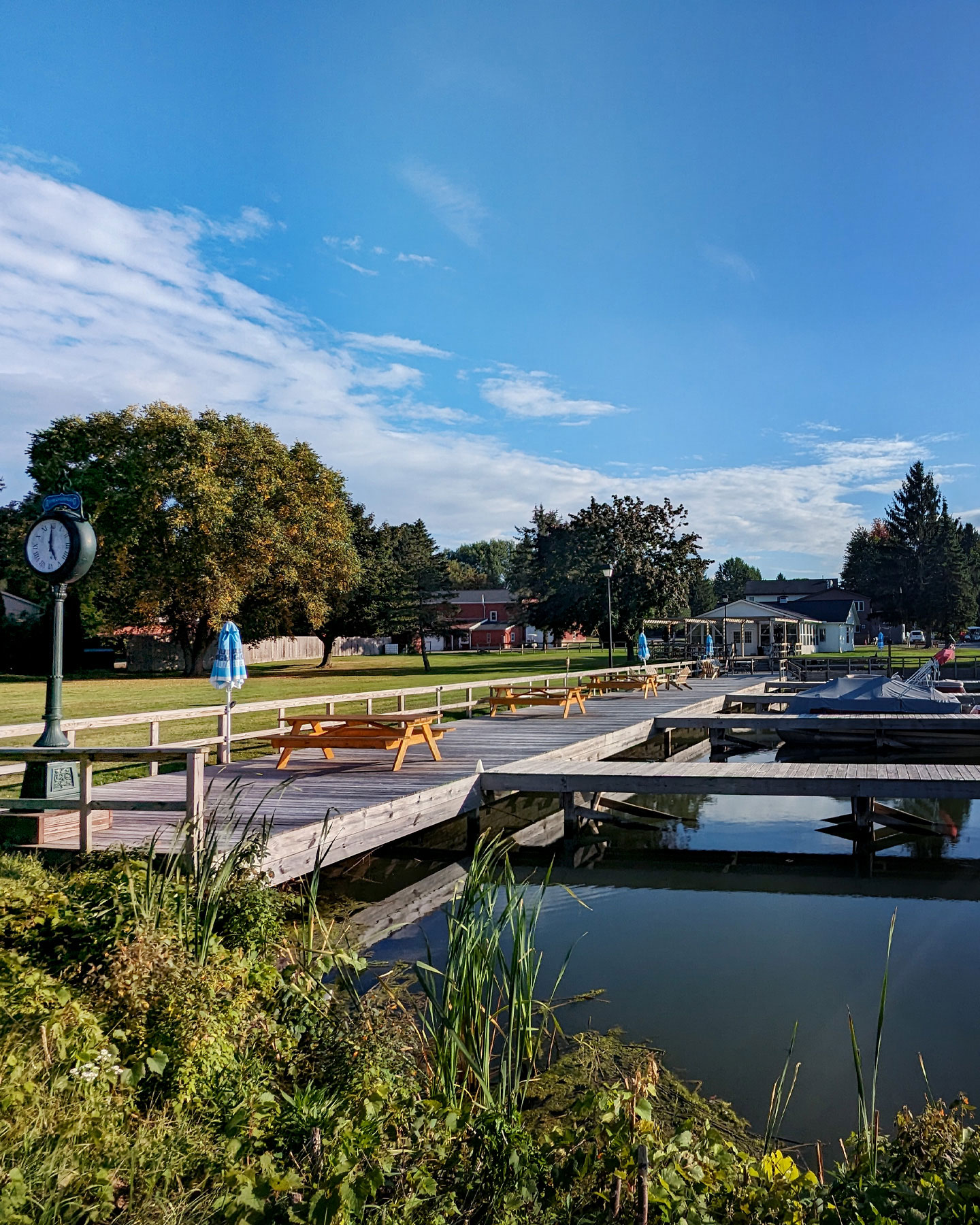 A canal with a dock and trees. A clock on a pole.