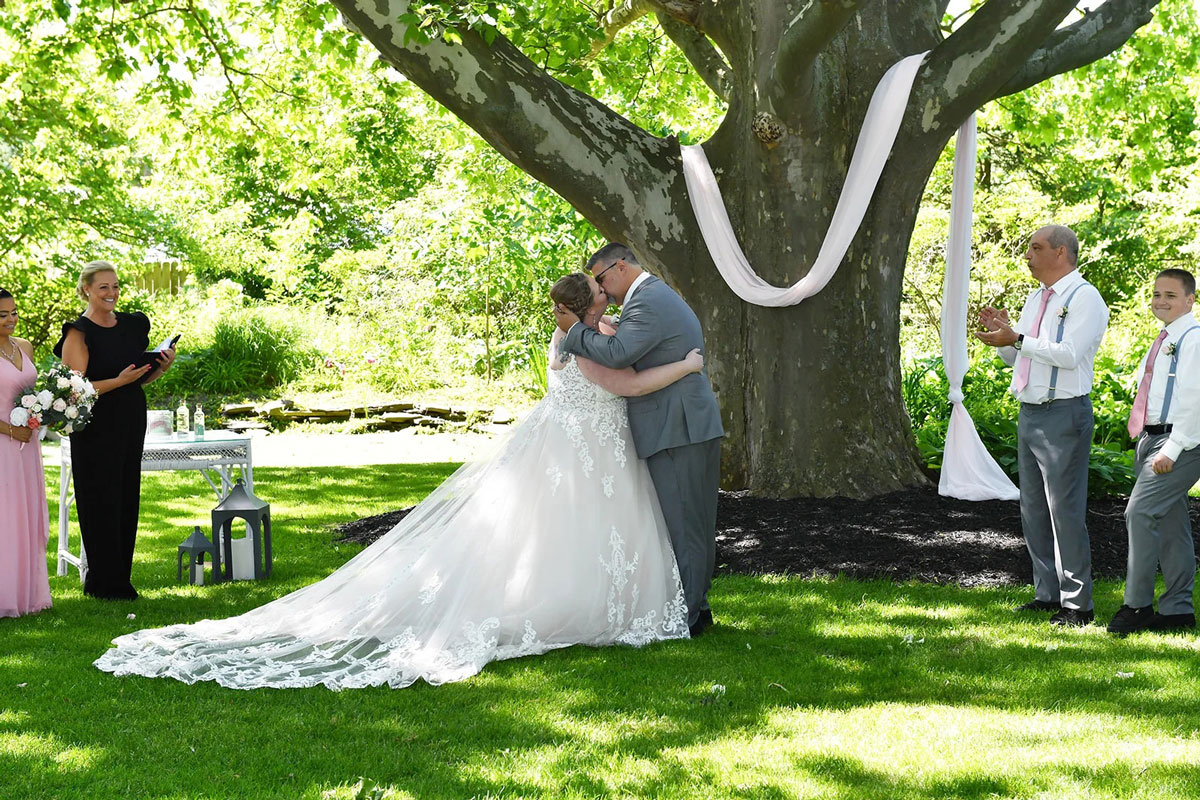 Bride and groom kissing. Wedding party standing by.