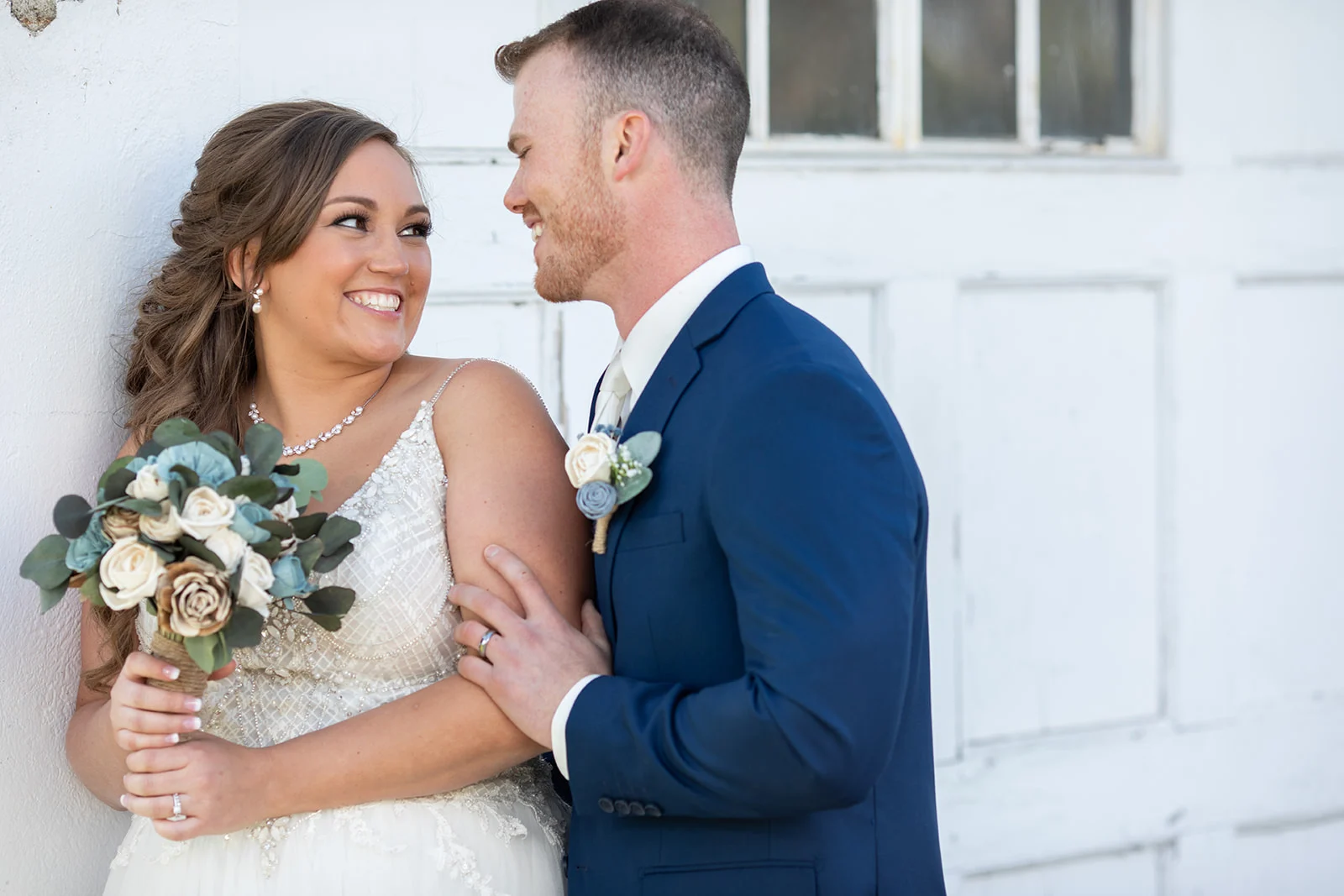 Happy bride and groom embracing. The bride is wearing a white wedding dress and holding flowers.