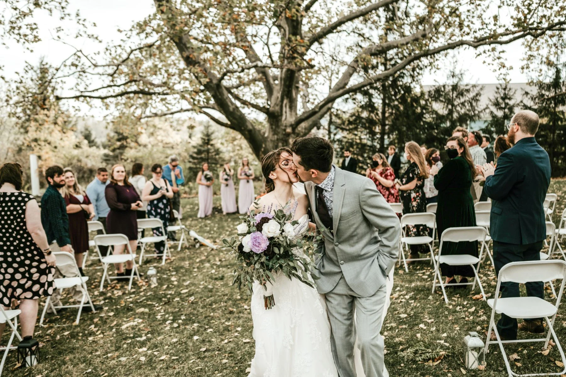 Bride and groom sharing a romantic kiss. Wedding party in background.