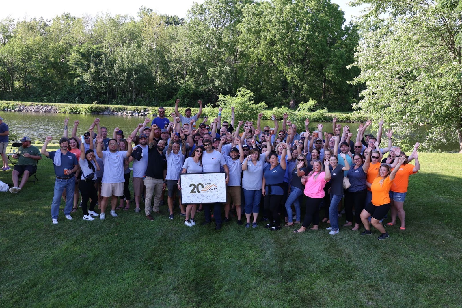 Large group of people standing on grass with a sign