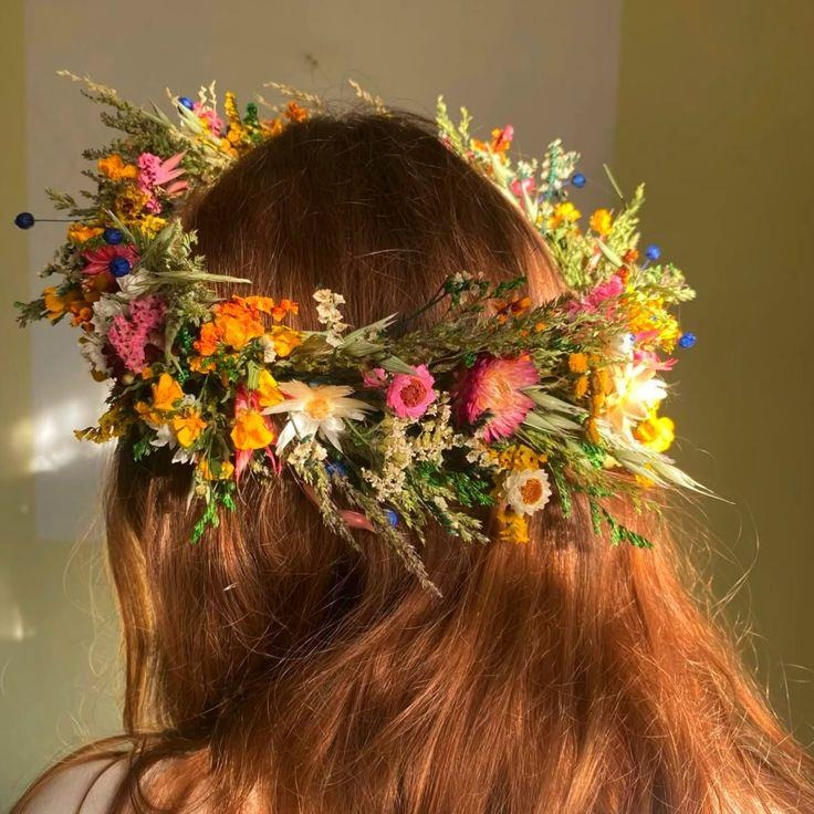 A woman wearing a vibrant floral crown on her head. The crown is made of colorful flowers and greenery.