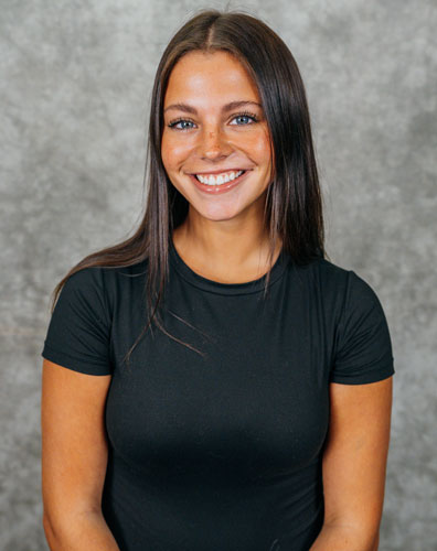 Portrait of a young woman with long dark hair. She is wearing a black t-shirt and smiling.