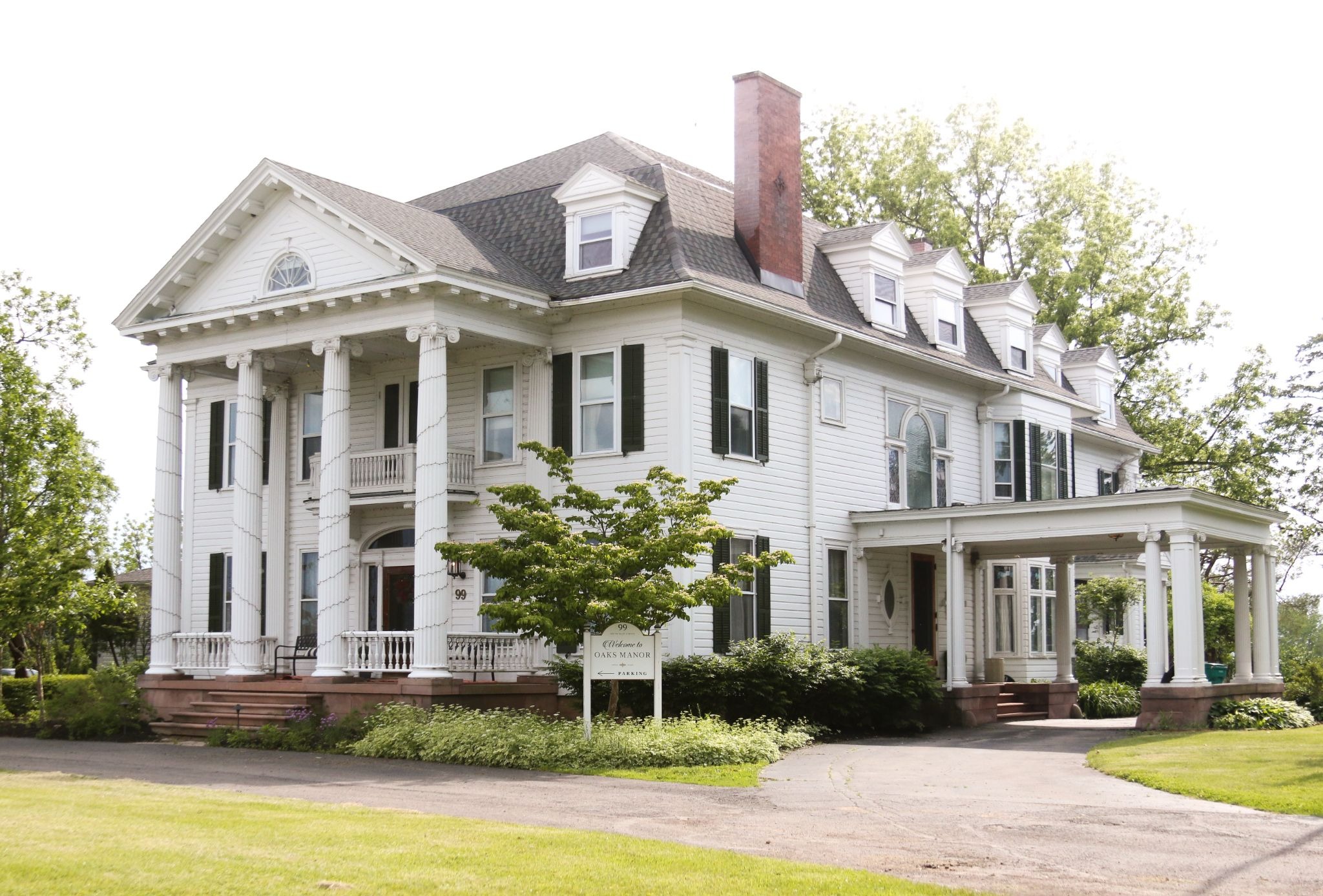 A large white colonial style house with columns and a chimney. The house has a well-manicured lawn.