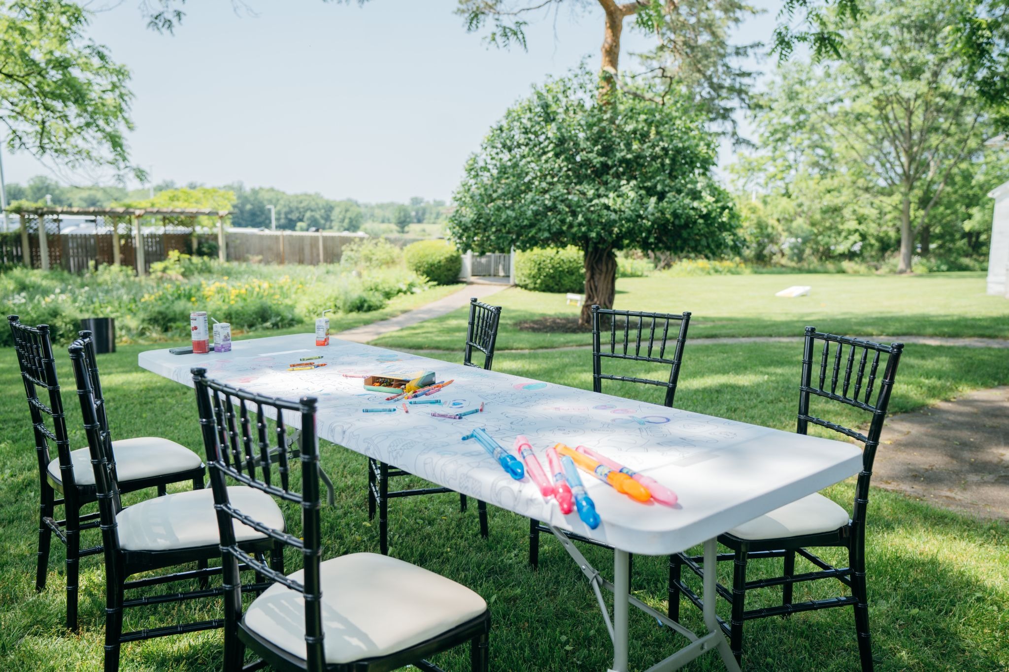 outdoor dining setup with black chairs and white tablecloths, vibrant napkins on the table. Colorful utensils and plates are set for a meal.