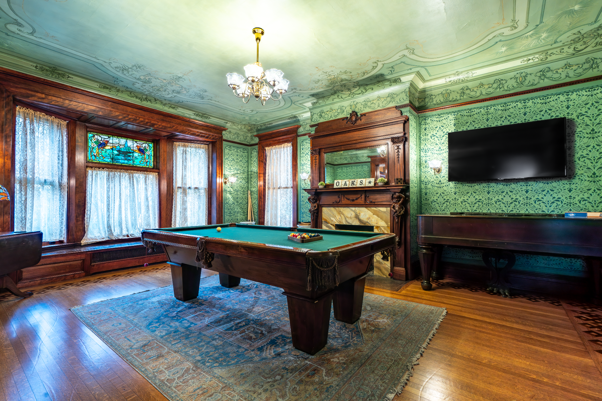 A classic billiard room with green walls and a hardwood floor. The room features a pool table and a large screen TV.