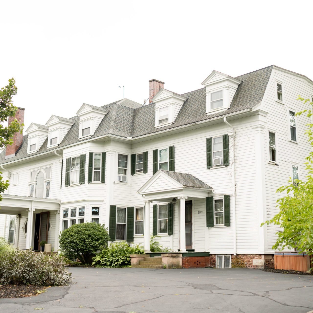 A large white house with green shutters and a driveway. The house has a gray roof.