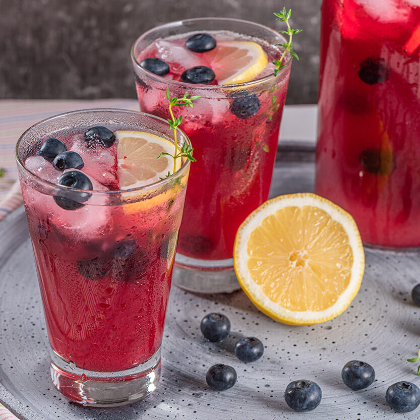 Refreshing glasses of blueberry lemonade. A pitcher in the background.