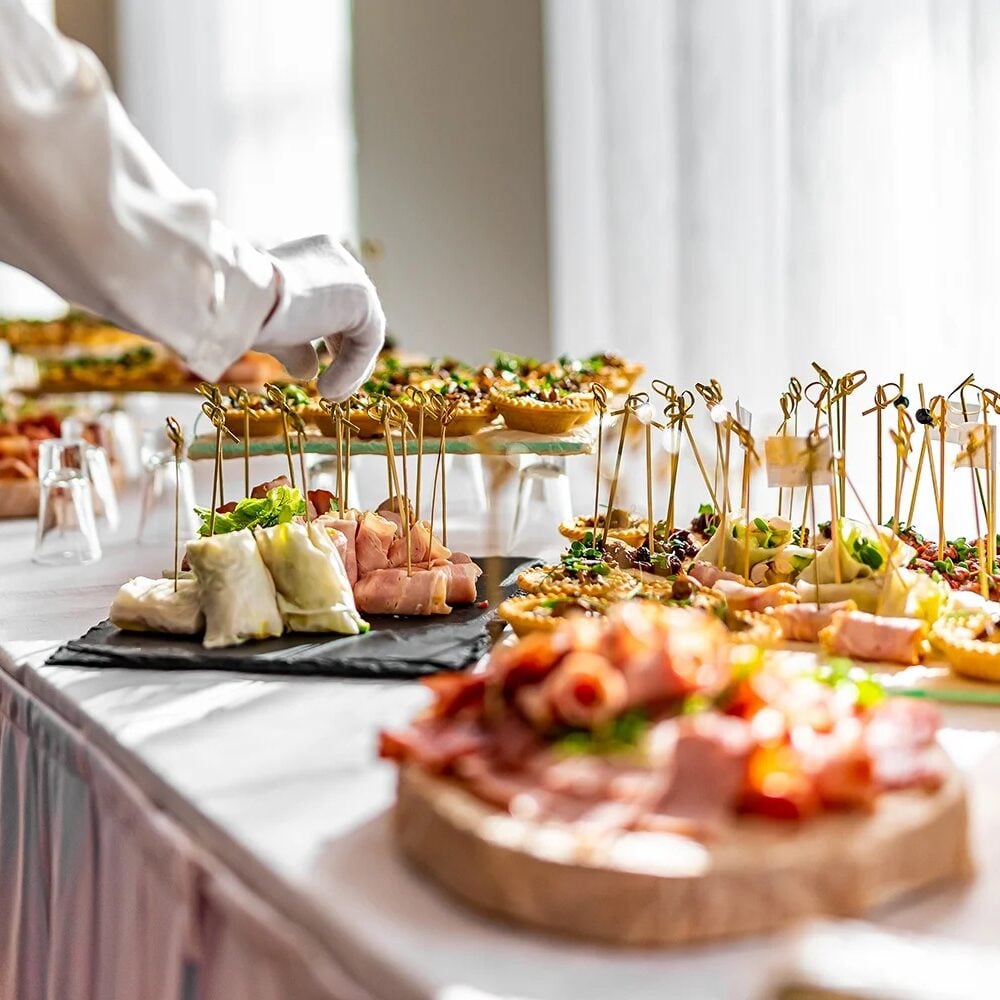 Catering staff member preparing dishes at a buffet table. Variety of food