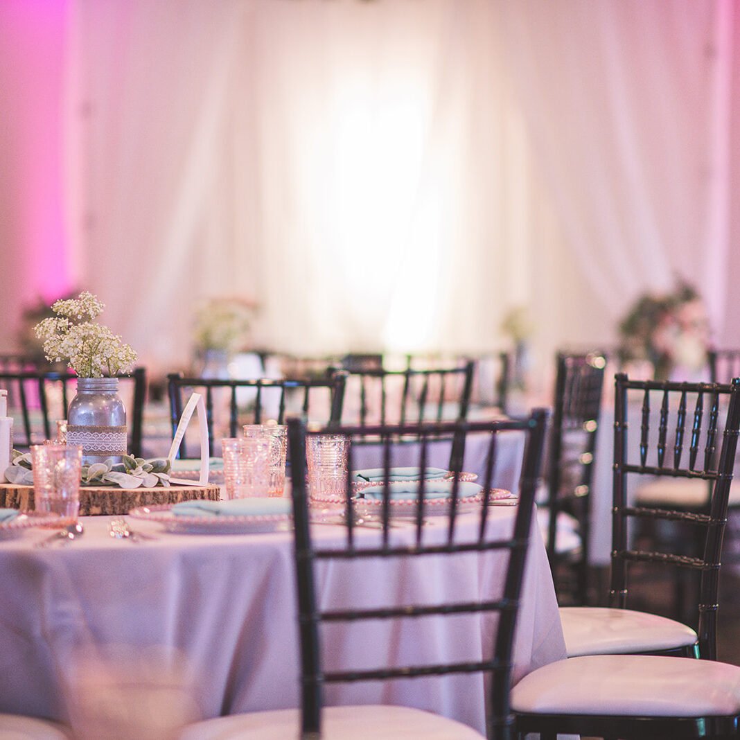 A beautifully set table with black chairs and pink lighting. The room is set for a formal event.